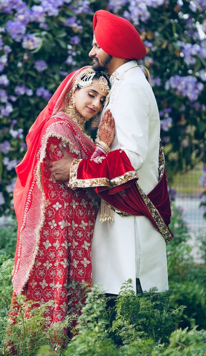 gallery-01 A couple embraces in vibrant traditional Indian clothing, surrounded by lush greenery.